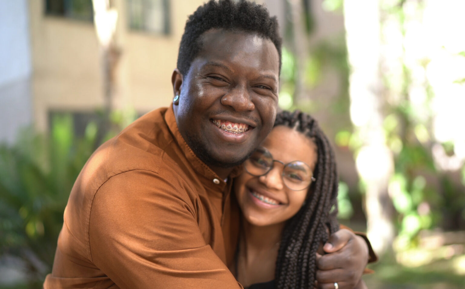 Brother and sister with braces hugging and smiling outside on a warm summer afternoon