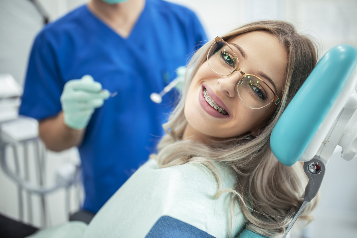 Teen with braces and glasses smiling while having her braces maintenanced by her orthodontist