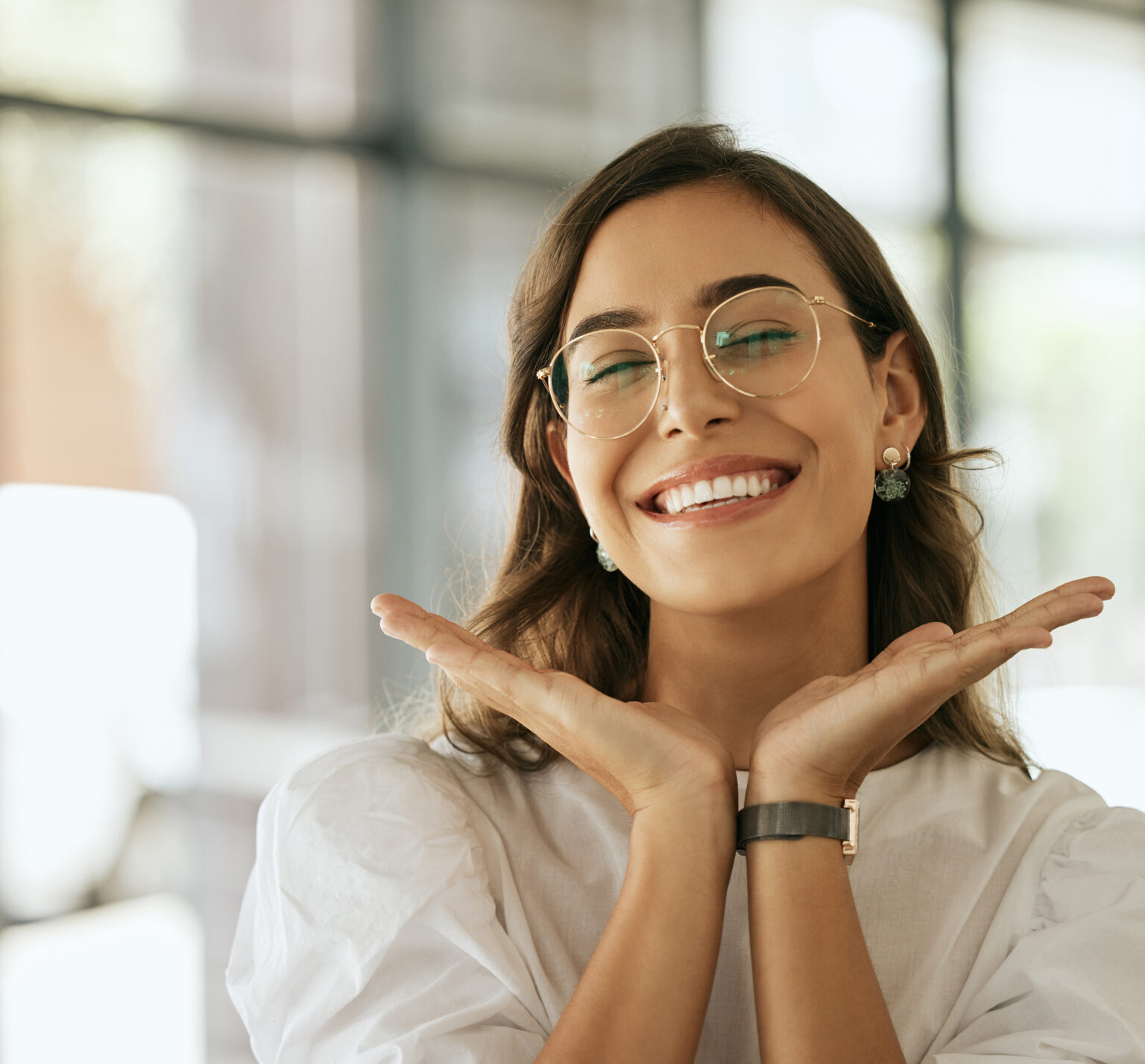 Cheerful Business Woman With Glasses Posing With Her Hands Under Her Face Showing Her Smile In An Office. Playful Hispanic Female Entrepreneur Looking Happy And Excited At Workplace
