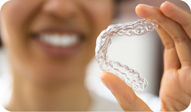Close up of an invisible aligner being held between the thumb and forefinger of a woman