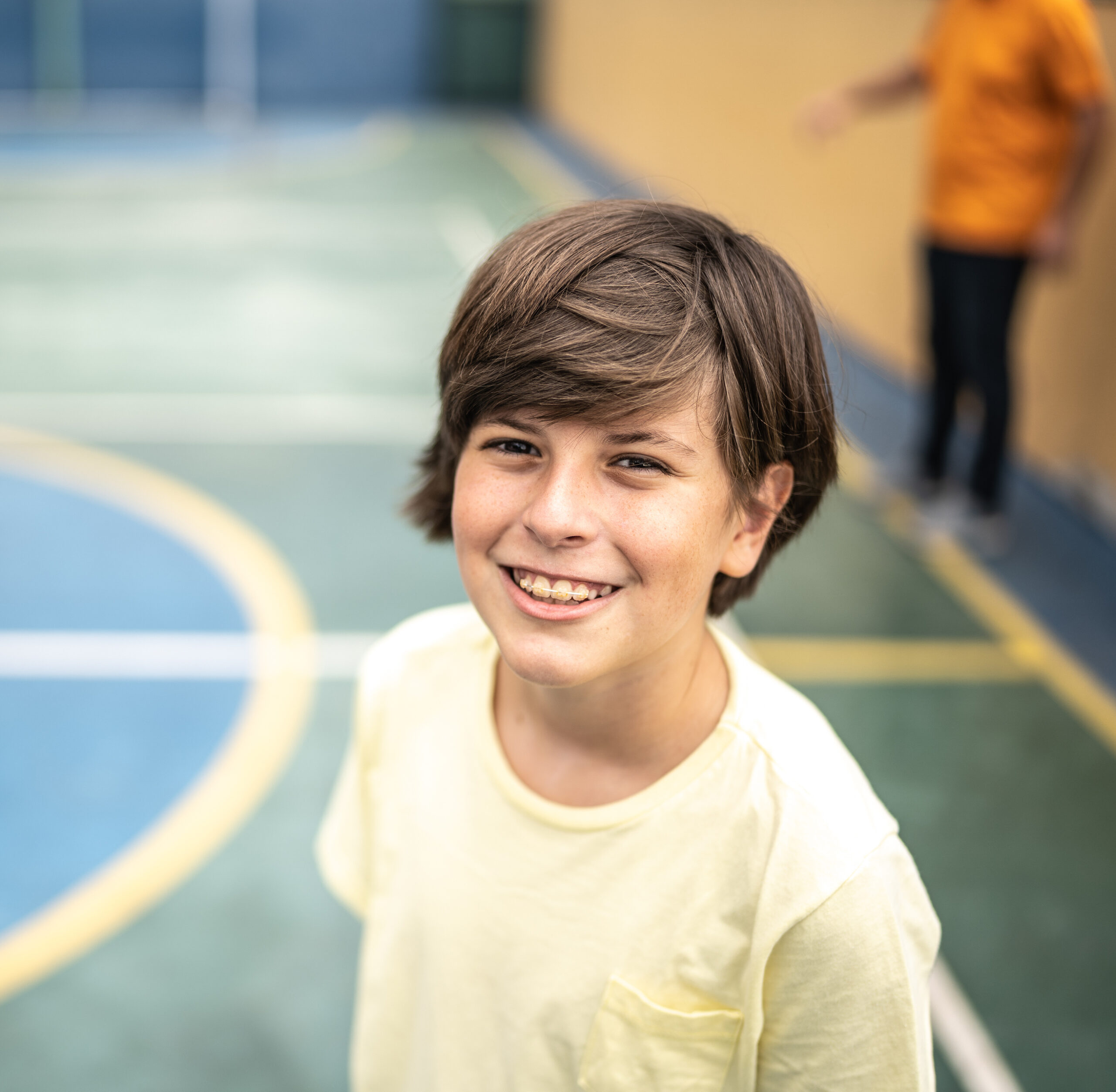 Close up of a young boy undergoing early orthodontics with clear braces, smiling on a small court