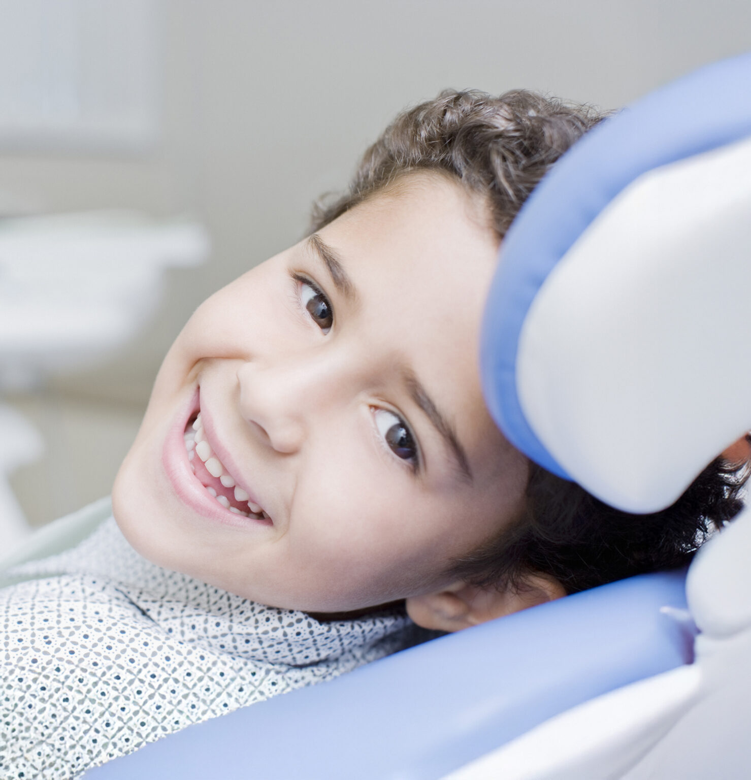 Close up of a small child in a white patterned button up smiling in the orthodontic treatment chair