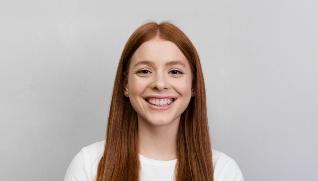 A red headed woman smiling, wearing a white tee shirt.