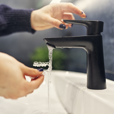 Close up a woman washing her clear plastic retainer in the sink