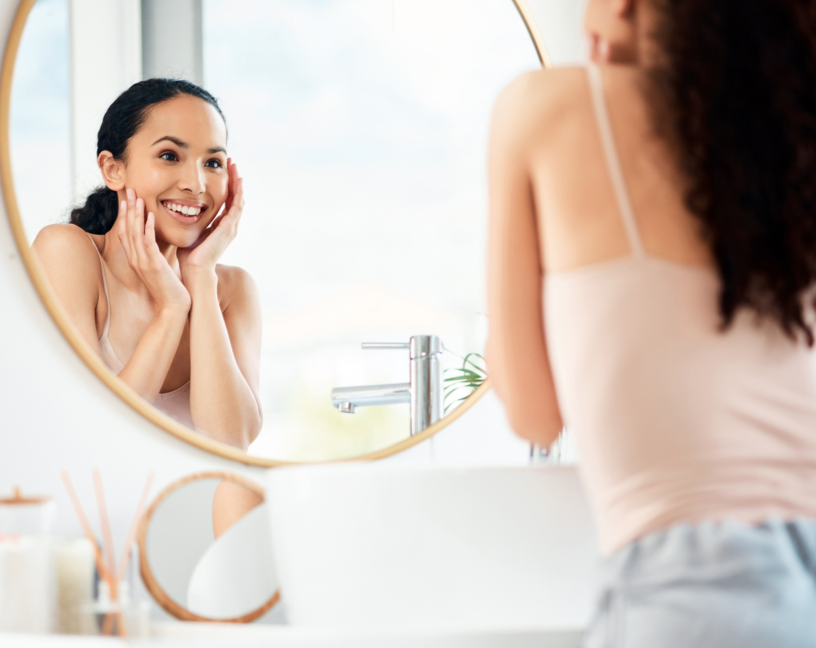 Woman excitedly examining her smile in the mirror after completing orthodontic treatment